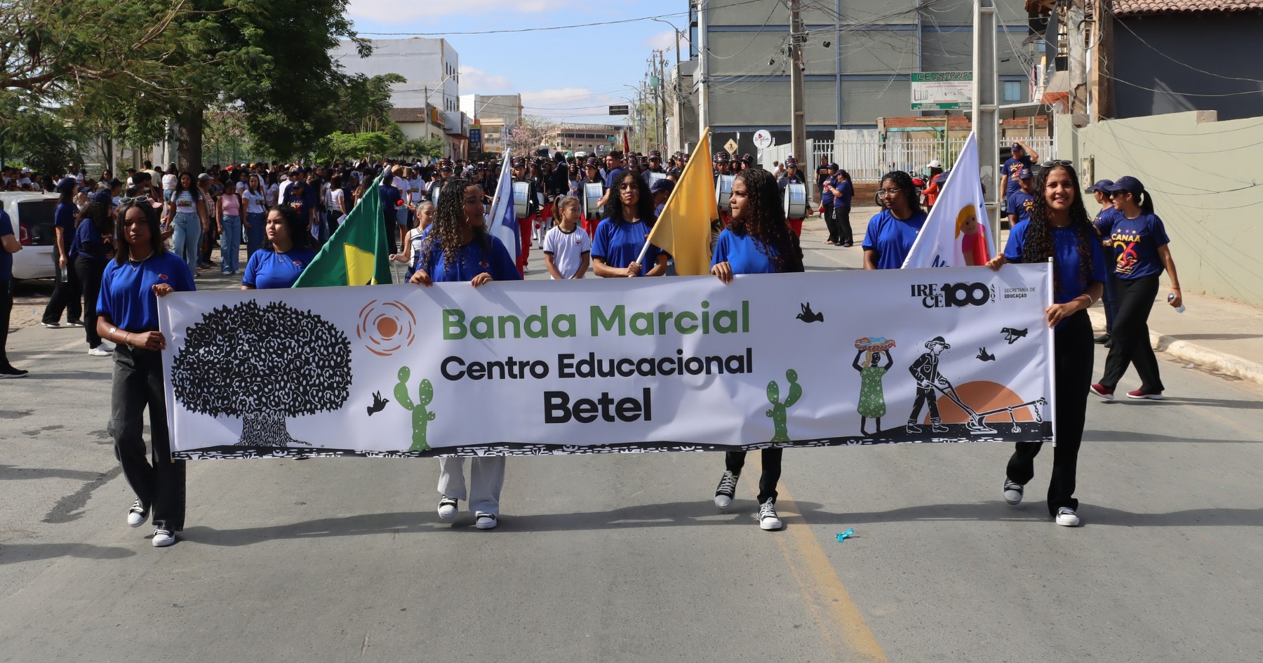 Estudantes carregam bandeiras e uma faixa com o nome Banda Marcial Centro Educacional Betel no desfile de 7 de Setembro em Irecê.