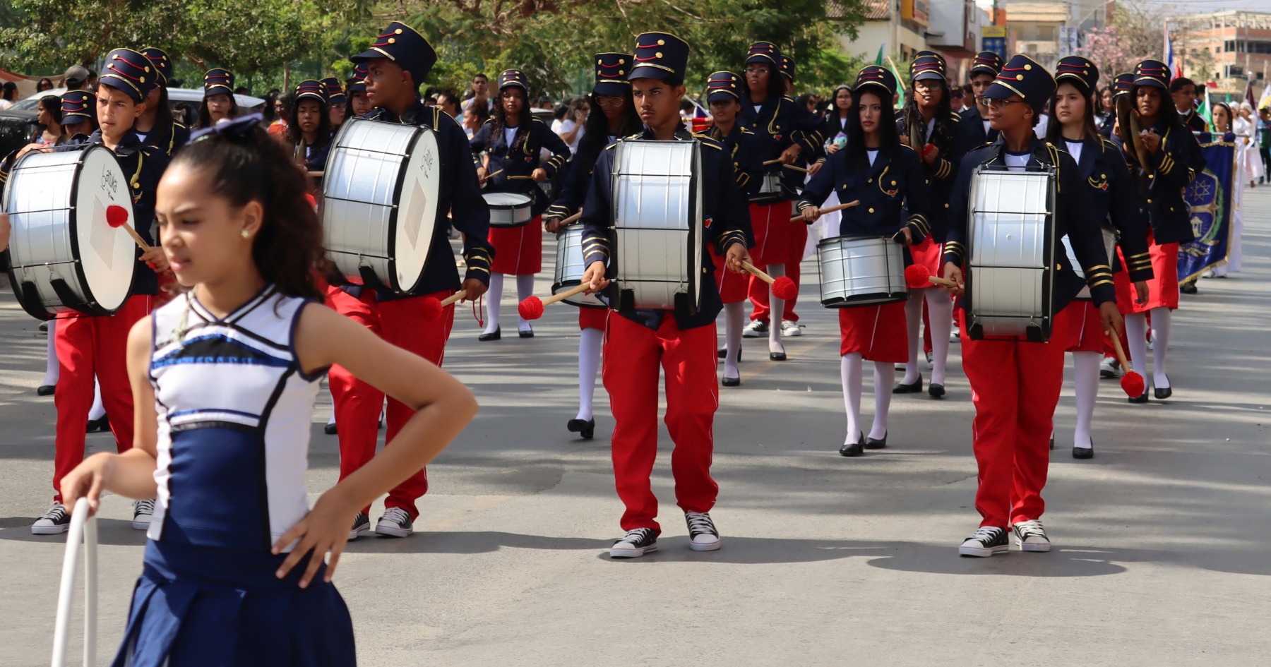 Alunos da Banda Marcial do Projeto Nova Canaã desfilam com instrumentos de percussão e uniformes azuis e vermelhos em Irecê.