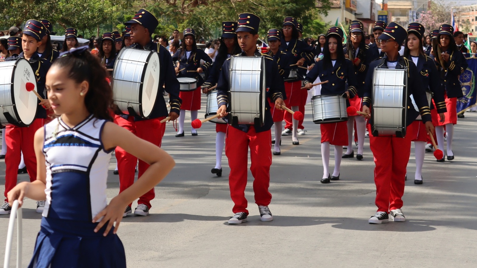 Alunos da Banda Marcial do Projeto Nova Canaã desfilam com instrumentos de percussão e uniformes azuis e vermelhos em Irecê.