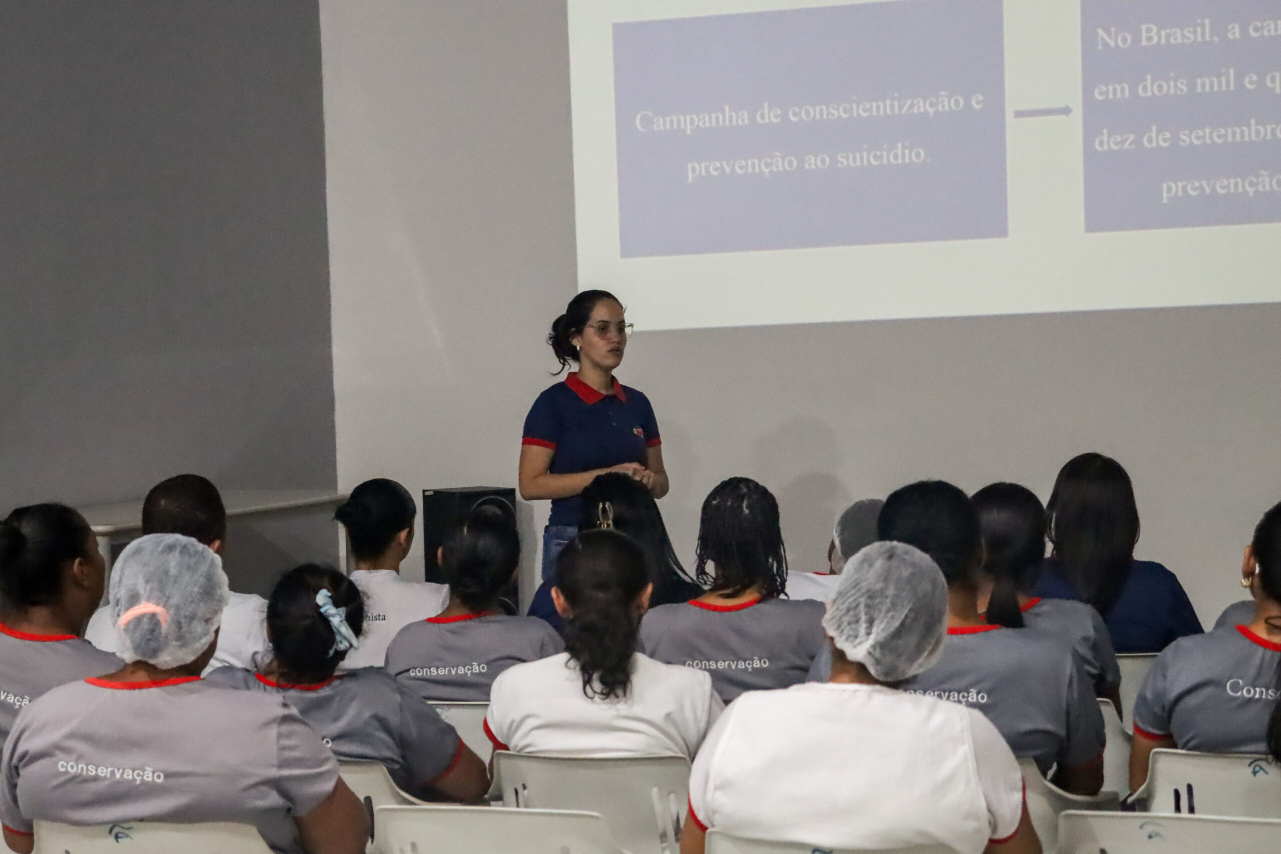 Participantes sentados acompanham uma apresentação com projeção sobre conscientização e prevenção ao suicídio.